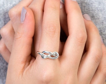 Op de afbeelding: Een zilveren knoop ring aan een vinger. De ring is een eenvoudig ontwerp met een knoop in het midden.
