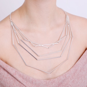 May include: A silver geometric necklace with multiple layers of interconnected bars forming a triangular shape.