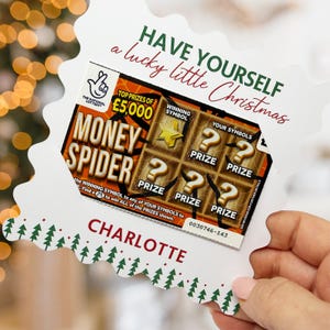 Könnte beinhalten: Eine weiße Karte mit Weihnachtsmotiv, die ein Lotterielos mit der Aufschrift "Money Spider" und dem Text "Have yourself a lucky little Christmas" zeigt. Die Karte ist mit dem Namen "Charlotte" personalisiert.
