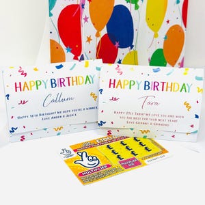 Könnte beinhalten: Zwei Geburtstagskarten mit der Aufschrift "Happy Birthday" in bunten Buchstaben. Eine Karte ist für Callum, die andere für Tara. Ein Lotterieschein liegt vor den Karten, mit dem Wort "Multiplikator" sichtbar.