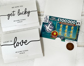 Puede incluir: Dos tarjetas blancas con el texto "We hope you get lucky" y "Lucky in love" con los nombres "Mr & Mrs Thomas" y la fecha "24.08.24". También se muestra un boleto de lotería con el texto "Top prizes of £100,000 £1 with a bonus game!"