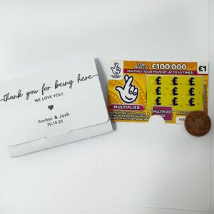 K&ouml;nnte beinhalten: Eine wei&szlig;e Karte mit dem Text "thank you for being here" und "WE LOVE YOU!" liegt neben einem Lotterielos und einem Penny. Das Lotterielos hat eine Multiplikatorfunktion und einen Hauptgewinn von 100.000 &pound;.