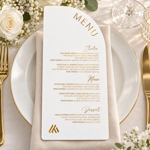 May include: An arched white menu card with gold foil lettering. The text includes sections for Starter, Main, and Dessert, listing dishes like salt-baked beetroot, stuffed bell pepper, and vanilla panna cotta, along with wine pairings and a logo.