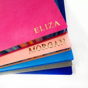 May include: A stack of colourful notebooks with personalised names, "ELIZA" and "MORGAN", in gold lettering.