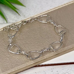 May include: A silver bracelet with a chain link design and multiple horse bit charms. The bracelet is on a light brown surface.