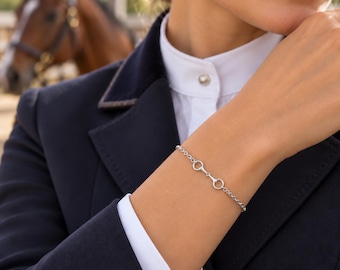 May include: A silver-coloured chain bracelet featuring a central equestrian bit link design. The bracelet is constructed with delicate circular links and a secure clasp, showcasing a polished metallic finish that rests against the wrist.