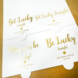 May include: Three white cards with gold foil lettering. The cards have the text "Get Lucky Tonight", "May you be Lucky!" and "Be Lucky Tonight". Each card has the text "Mr & Mrs Dalton 19.06.24" at the bottom.