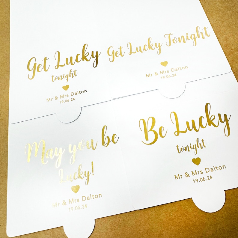 May include: Three white cards with gold foil lettering. The cards have the text "Get Lucky Tonight", "May you be Lucky!" and "Be Lucky Tonight". Each card has the text "Mr & Mrs Dalton 19.06.24" at the bottom.