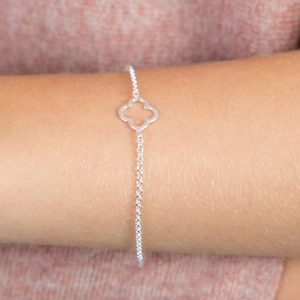 Puede incluir: Una pulsera de plata con una cadena delicada y un dije de trébol de cuatro hojas.