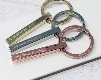 May include: Three gold, silver, and rose gold bar keychains with engraved text. The text on the gold keychain reads "Graduated 2023 Liverpool University". The text on the silver keychain reads "Lucy Smith BSc (Hons)". The text on the rose gold keychain reads "Love Mum & Dad x".