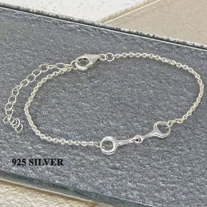 Puede incluir: Un brazalete de plata con un dise&ntilde;o de bocado de caballo. El brazalete tiene un dise&ntilde;o de cadena con un cierre de mosquet&oacute;n y una cadena ajustable. El texto "925 SILVER" es visible.
