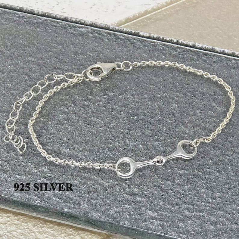 Puede incluir: Un brazalete de plata con un dise&ntilde;o de bocado de caballo. El brazalete tiene un dise&ntilde;o de cadena con un cierre de mosquet&oacute;n y una cadena ajustable. El texto "925 SILVER" es visible.