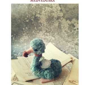 Puede incluir: Un juguete de peluche azul en forma de dodo con un pico marrón y una silla de montar azul claro. El juguete está sentado en una pila de libros antiguos con texto en un idioma extranjero.