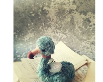 May include: A plush blue dodo bird toy with a brown beak and a light blue saddle. The toy is sitting on a stack of old books with text in a foreign language.