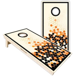 May include: Two wooden cornhole boards with a cream-colored surface and a black border. The boards feature a honeycomb design in orange and black. Each board has a centered hole for bean bag toss.