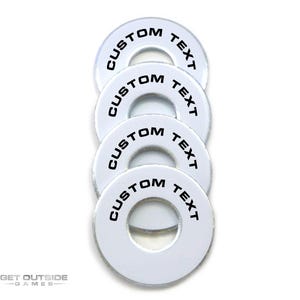 May include: Four white, circular game pieces with a hole in the center. Each piece has the words "CUSTOM TEXT" printed in black around the edge. The pieces are stacked vertically against a white background.