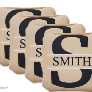 May include: Four tan bean bags with the letter "S" in black and the name "SMITH" in white. The bean bags are rectangular and appear to be made of a soft fabric. The bean bags are for a game.