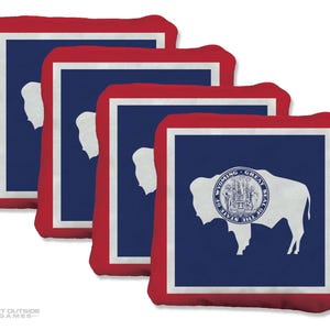 Könnte beinhalten: Vier quadratische Ziele für das Bean Bag Toss-Spiel. Jedes Ziel zeigt das Design der Flagge des Bundesstaates Wyoming mit einem roten Rand, einem weißen Innenrand und einer blauen Mitte. Das Staatssiegel von Wyoming ist auf einem der Ziele abgebildet.