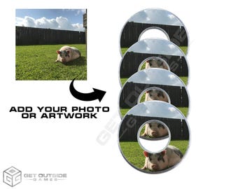 Könnte beinhalten: Kreisförmige Spielsteine mit einem Schweinebild in der Mitte, umgeben von einer Rasenfläche und einem Holzzaun unter einem bewölkten Himmel. Der Text "ADD YOUR PHOTO OR ARTWORK" ist zu sehen. Das Logo von "GET OUTSIDE GAMES" ist ebenfalls sichtbar.