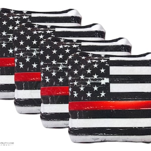 May include: Four cornhole bags with a distressed American flag design. The bags feature a black and white flag with a red stripe, and white stars on a black background. The bags are likely for outdoor games.