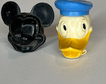 Peut inclure: Deux figurines de personnages en plastique vintage, Mickey Mouse et Donald Duck. Mickey Mouse est noir avec de grandes oreilles et un nez noir. Donald Duck est blanc avec un bec jaune et un chapeau de marin bleu.