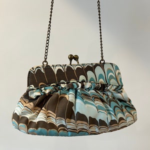 May include: A brown and blue patterned clutch purse with a gold chain strap. The purse has a ruffled edge and a clasp closure.