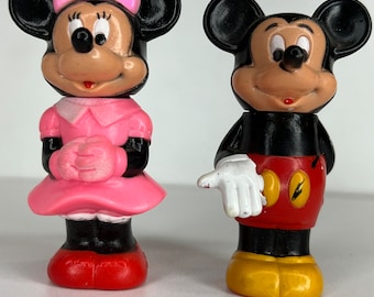 Peut inclure: Une paire de figurines en plastique vintage de Mickey Mouse et Minnie Mouse. Mickey porte un short rouge avec des chaussures jaunes et des gants blancs. Minnie porte une robe rose avec des chaussures rouges et un nœud rose.