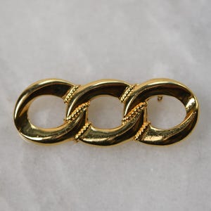 Può includere: Un fermaglio a forma di catena con tre maglie dorate.