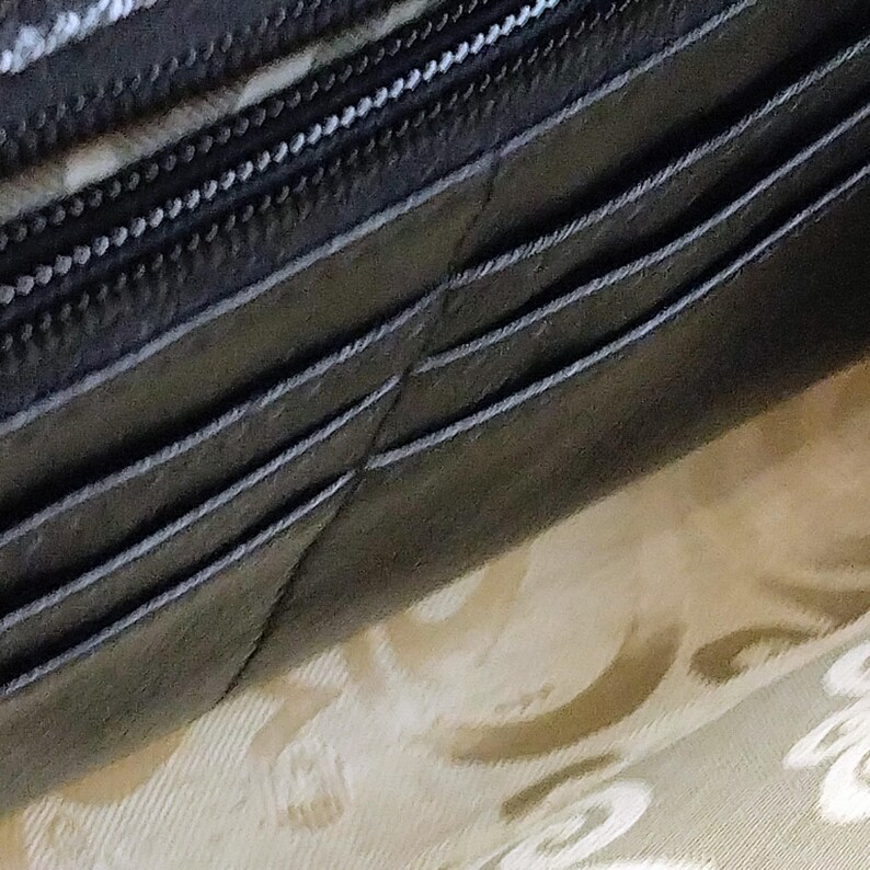 Puede incluir: Primer plano de una cartera de cuero marr&oacute;n oscuro con costuras blancas y una cremallera. La cartera parece estar parcialmente abierta, revelando un interior estampado. El cuero tiene un aspecto ligeramente texturizado.