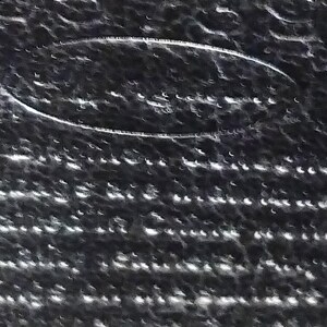 Puede incluir: Primer plano de una superficie texturizada de color gris oscuro con un dise&ntilde;o ovalado blanco. La superficie tiene un patr&oacute;n de peque&ntilde;os puntos blancos irregulares, creando un efecto moteado. El dise&ntilde;o ovalado parece ser un logotipo o emblema en relieve.