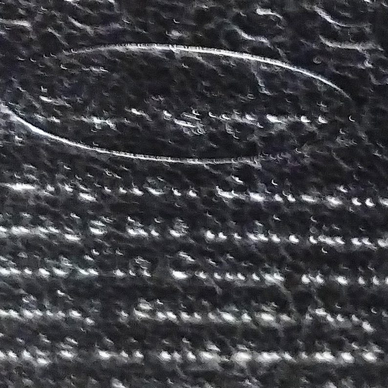 Puede incluir: Primer plano de una superficie texturizada de color gris oscuro con un dise&ntilde;o ovalado blanco. La superficie tiene un patr&oacute;n de peque&ntilde;os puntos blancos irregulares, creando un efecto moteado. El dise&ntilde;o ovalado parece ser un logotipo o emblema en relieve.