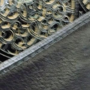 Puede incluir: Primer plano de un elemento arquitect&oacute;nico decorativo con intrincados patrones arremolinados en tonos dorados y grises. El dise&ntilde;o presenta una superficie texturizada con una l&iacute;nea diagonal de formas repetitivas detalladas.