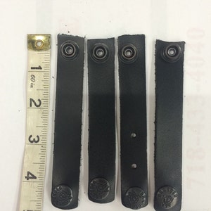 Puede incluir: Cuatro correas de cuero negro con anillos de metal y un logotipo negro que dice "Branded" en cada correa.