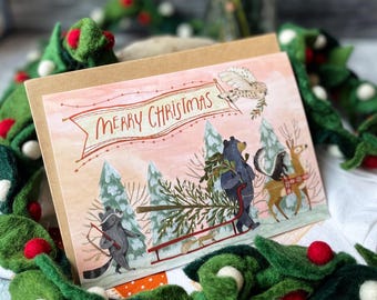 May include: A Christmas card with a pink and orange background featuring a group of animals pulling a Christmas tree on a sled. The animals include a bear, a raccoon, a skunk, and a deer. The card has the text "Merry Christmas" in red and white.