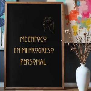 Könnte beinhalten: Ein gerahmter schwarzer Druck mit goldenem Text und einer Strichzeichnung eines Frauengesichts. Der Text lautet "ME ENFOCO EN MI PROGRESO PERSONAL". Rechts vom Rahmen steht eine weiße Vase mit getrockneten Zweigen.