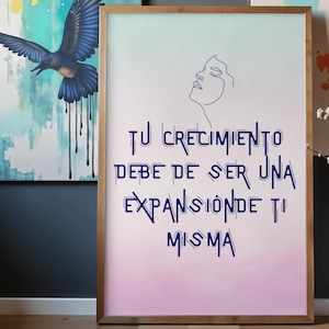 Könnte beinhalten: Ein gerahmter Druck mit einem Farbverlaufshintergrund aus Hellblau und Rosa. Der Druck zeigt eine Strichzeichnung eines Frauengesichts und den Text "TU CRECIMIENTO DEBE DE SER UNA EXPANSION DE TI MISMA" in Dunkelblau. Im Hintergrund befindet sich ein Gemälde eines blauen Vogels.