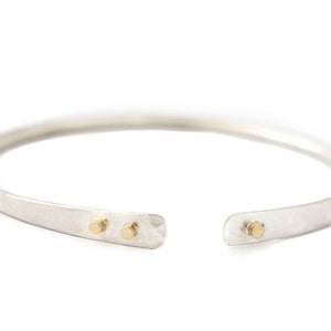 May include: A silver bangle bracelet with two small gold accents.