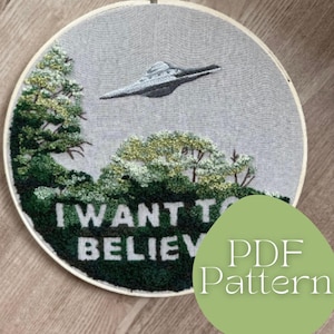 Puede incluir: Arte de aro bordado con un OVNI volando sobre un bosque. El texto "I WANT TO BELIEVE" está bordado en blanco sobre un fondo verde oscuro. El diseño incluye un patrón PDF.