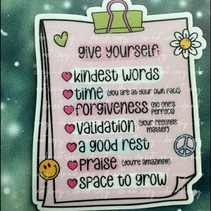 May include: A pink checklist with a green paperclip at the top. The checklist has a white daisy at the top right corner and a heart at the top left corner. The checklist says "Give yourself: Kindest words, Time (you are at your own pace), Forgiveness (no one's perfect), Validation (your feelings matter), A good rest, Praise (you're amazing!), Space to grow."