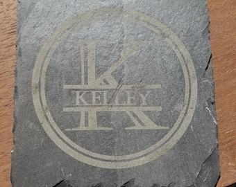 May include: A black slate coaster with a white circle design featuring the letters "K" and "R" intertwined with the word "KELLEY" in the center.