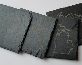 May include: Four gray slate coasters with an etched outline of the state of Michigan. The coasters are stacked on top of each other.