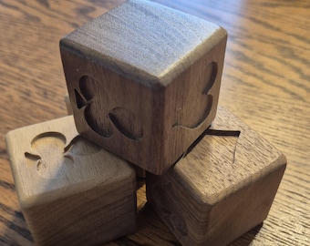 May include: Three wooden cubes crafted from dark brown walnut wood, each featuring a different engraved card suit symbol on its face. The cubes are stacked in a cluster, displaying visible wood grain patterns and smooth, sanded edges on all sides.