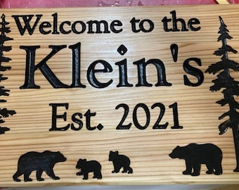 May include: A wooden sign with the text "Welcome to the Klein's Est. 2021" carved into it. The sign is decorated with two pine trees and three bears.