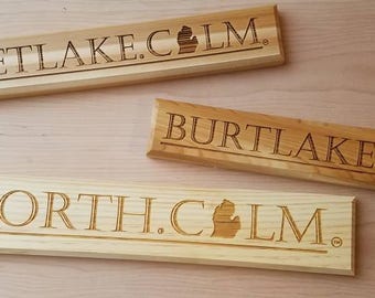 May include: Three wooden signs with the text "Mulletlake.clm", "Burtlake.clm", and "Upnorth.clm" with a stylized outline of the state of Michigan.