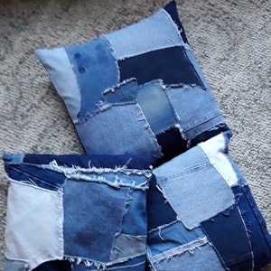 May include: Three blue denim patchwork throw pillows with frayed edges. The pillows are made from different shades of blue denim and have a rustic, handmade look.