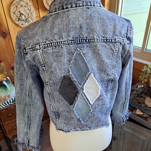 May include: A light blue denim jacket with a diamond pattern on the back. The diamonds are made of different shades of blue, black, and white denim.