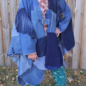 May include: A woman wearing a denim patchwork poncho with a floral print top and teal leggings. She is standing in front of a wooden fence and wearing black sneakers.
