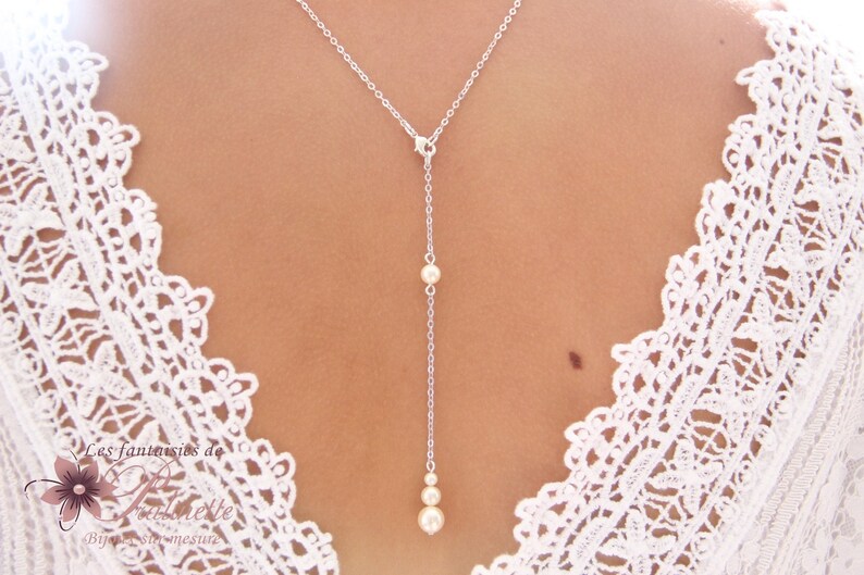 May include: A silver chain necklace with three white pearls hanging from it. The necklace is on a model wearing a white lace top.
