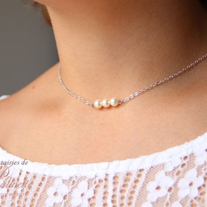 May include: A silver chain necklace with three white pearls. The necklace is on a person's neck.