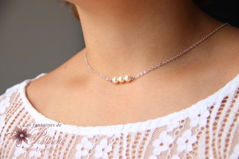 May include: A silver chain necklace with three white pearls. The necklace is on a person's neck.